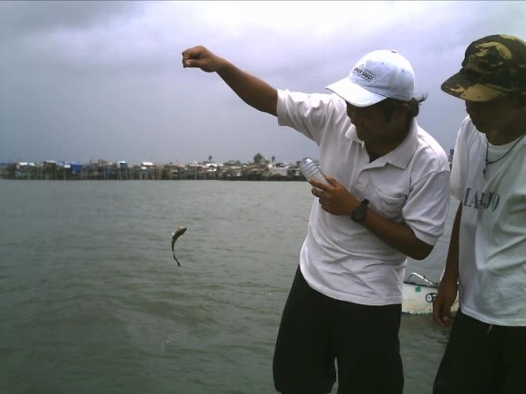 two men are standing in front of the water and fishing