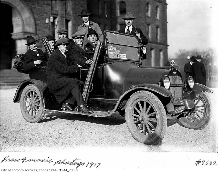 a group of men in suits and ties sit behind an old car