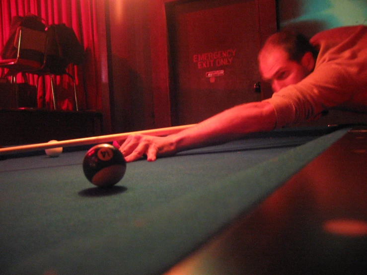 the man leans forward to play billiard's cue
