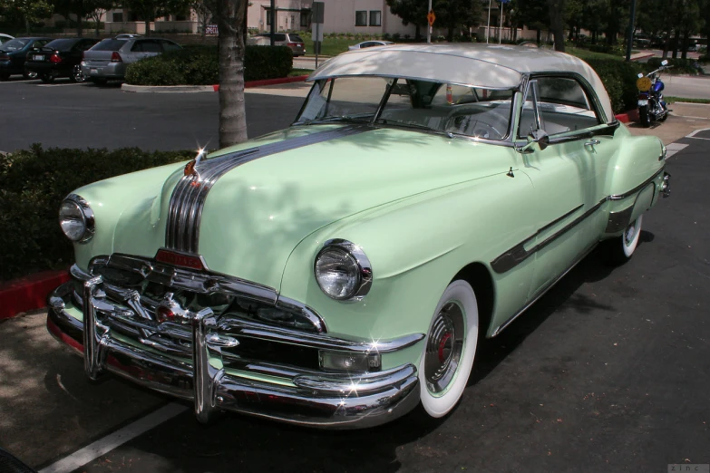 an old green car is parked in a parking lot