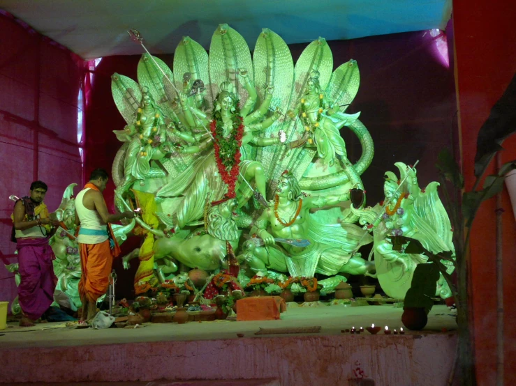 men are standing behind a big green statue