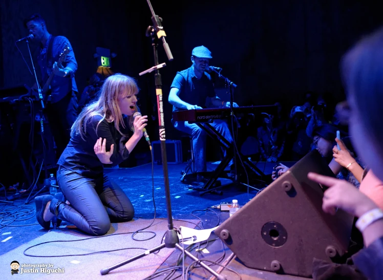 a woman kneeling down and reading on stage