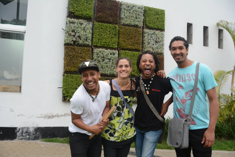 three people smiling for the camera with a grass wall behind them