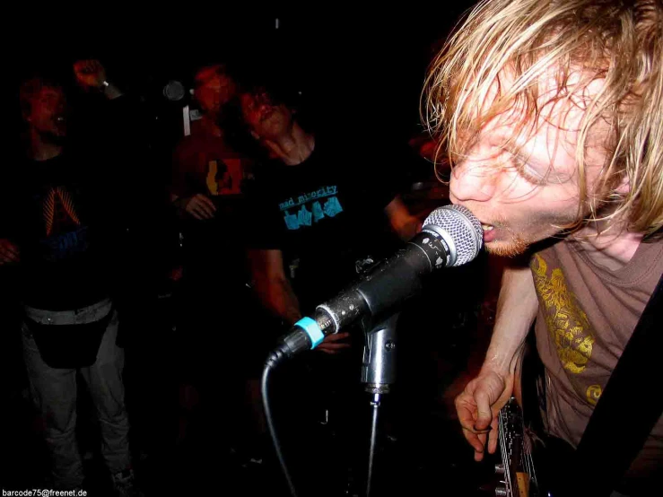 a man singing into a microphone while a band watches