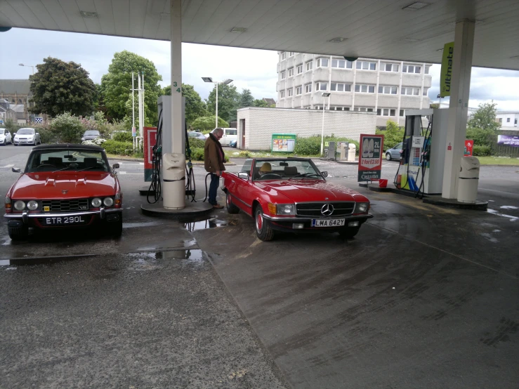 red cars at a gas station with people filling them up