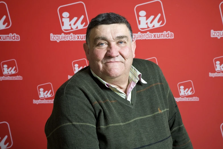 a man in green sweater standing in front of a red backdrop