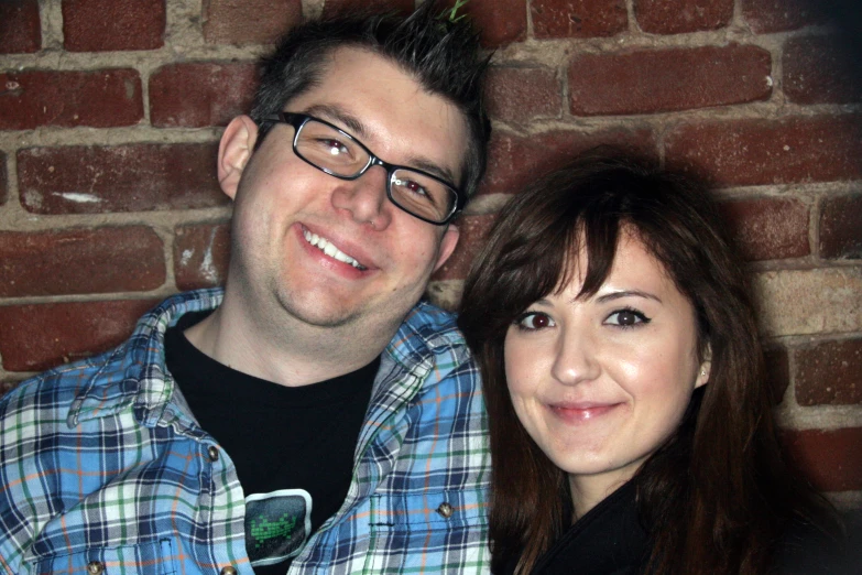 a young woman standing next to a man against a brick wall