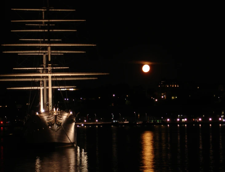 a ship floating in the night with a moon behind it