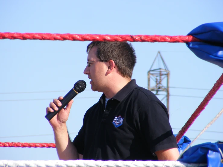 the man is talking into a microphone in front of ropes