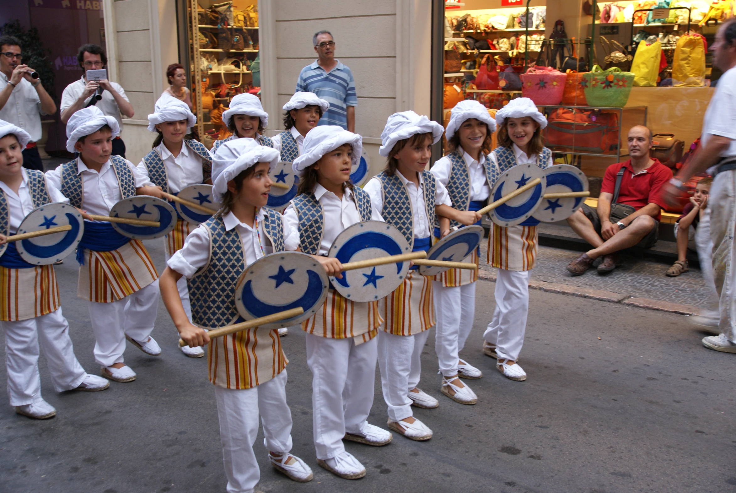 young children wearing uniforms holding their large drums in one hand