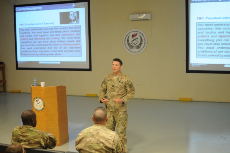 two soldiers standing at a podium in front of a man speaking