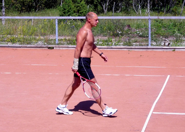 a bald man holding a tennis racket and ball