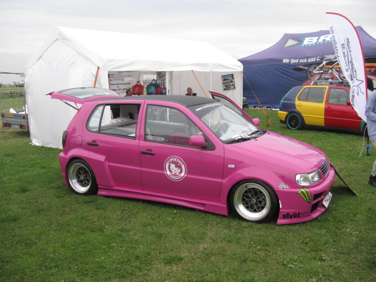 pink car with its hood lifted on a grassy field