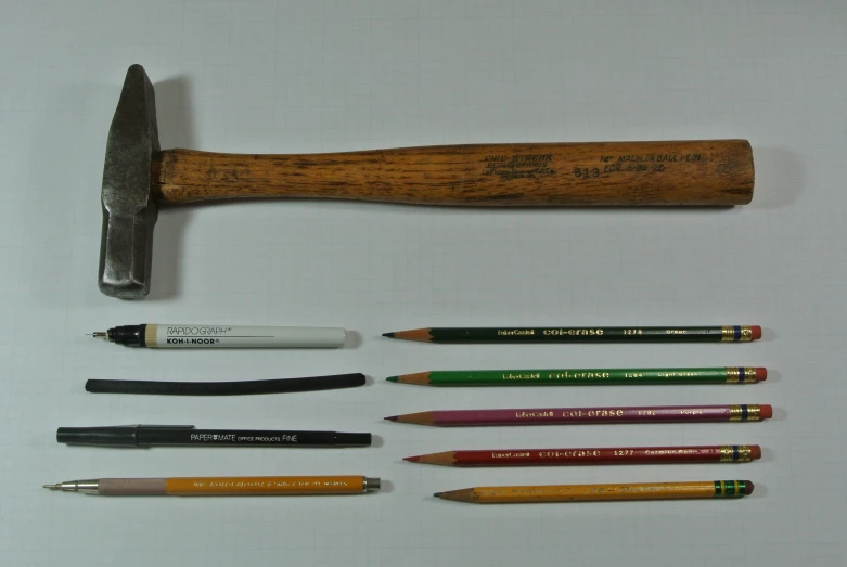 several pens and a hammer, next to a piece of wooden