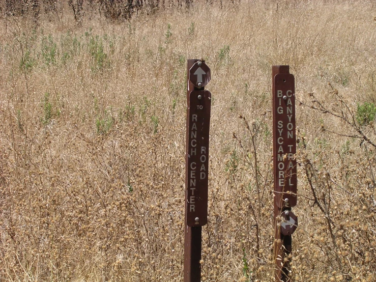 two rusted metal signs sitting in a field