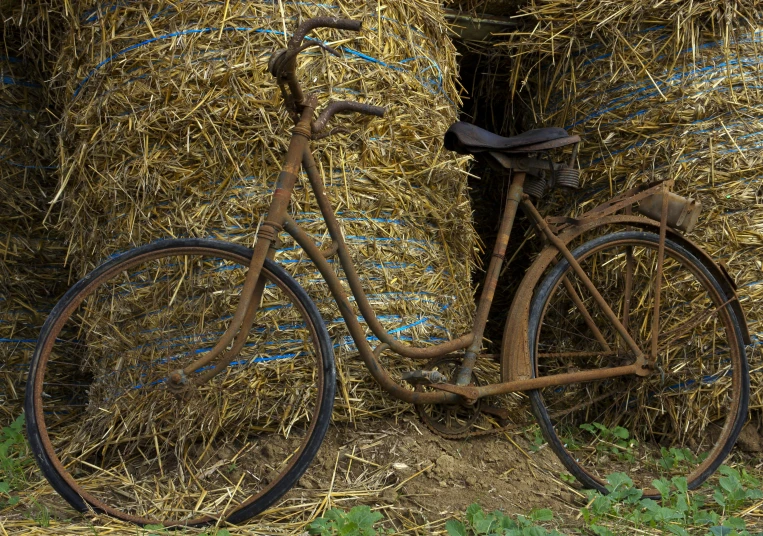 a very old rusty bike parked next to a bunch of hay