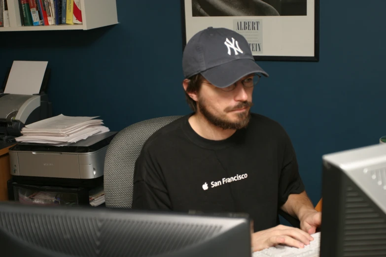 a man in a baseball hat looks at a computer