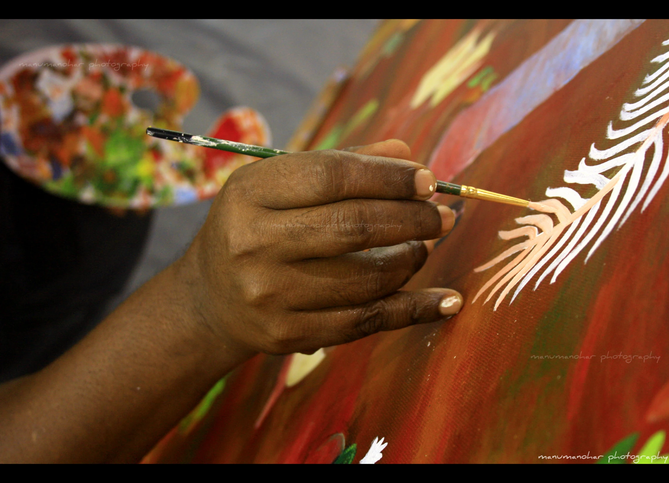 someone draws an feather on a red, yellow and green painting