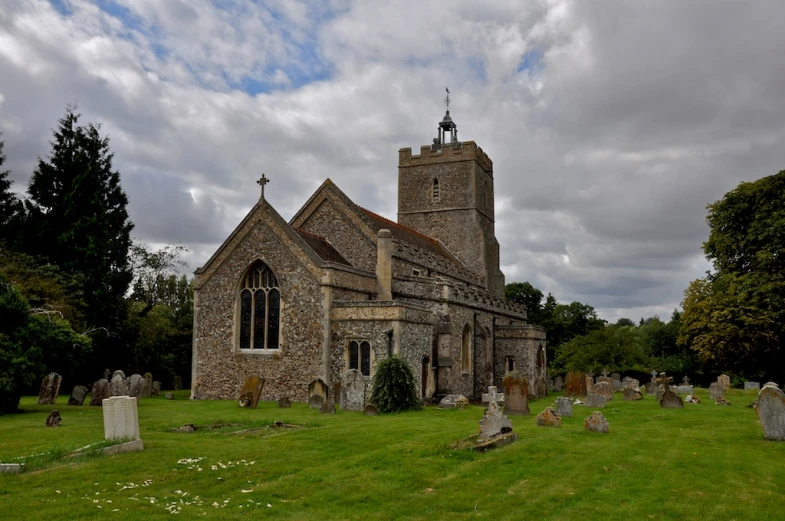 a gothic stone church stands surrounded by graves and green grass