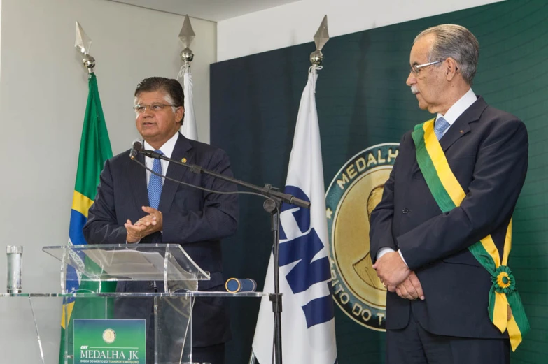 two men standing at a podium with flags in the background