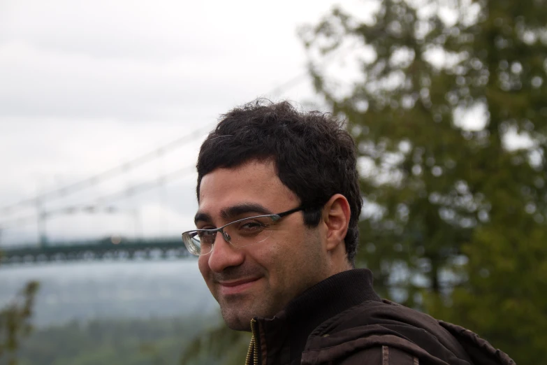 a man in glasses smiling while standing by some trees