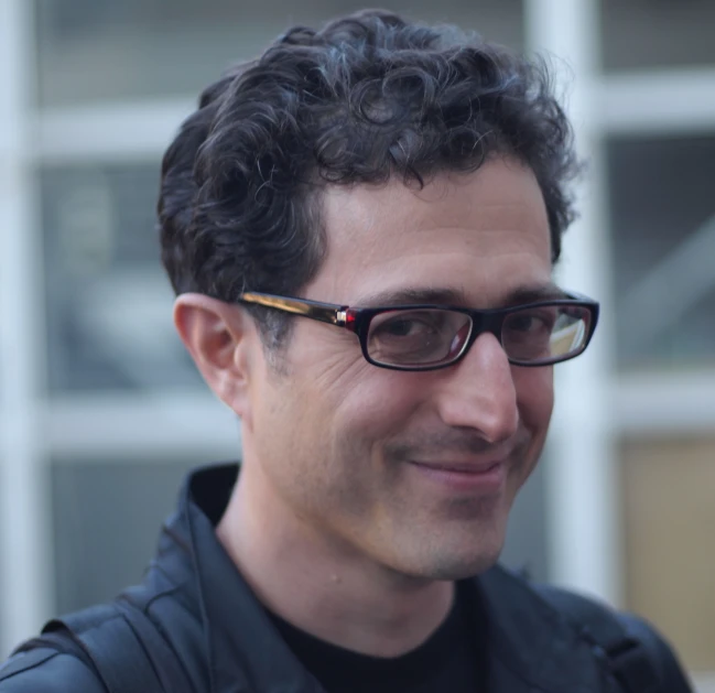 a man with curly hair in glasses smiling