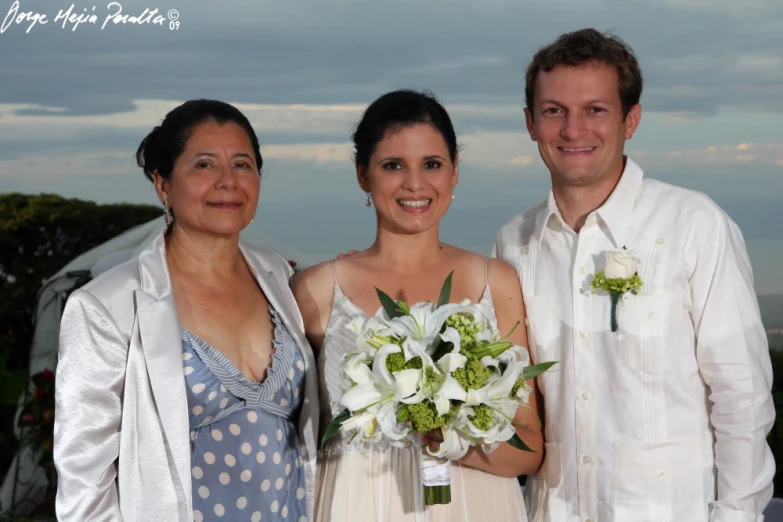 three people standing together while one person in a white shirt holds flowers