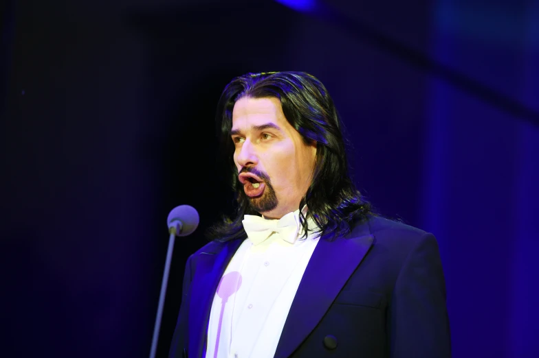 a man in a tuxedo is making an speech into a microphone