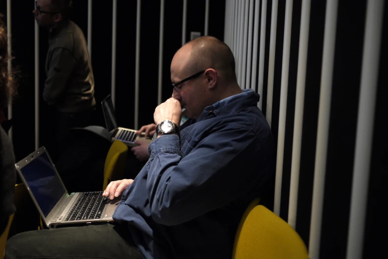 two men working on laptops in front of a wall