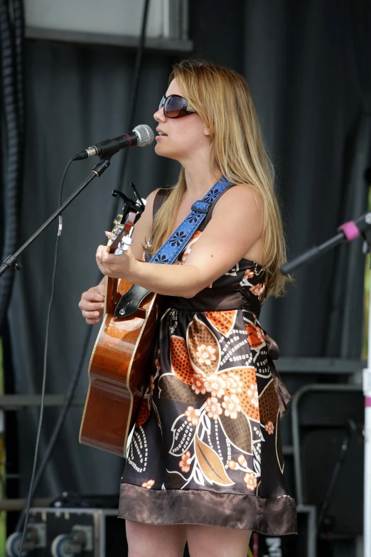 a woman wearing sunglasses and singing at an outdoor concert