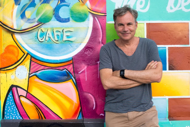 a man leaning against a colorful wall with his arms crossed