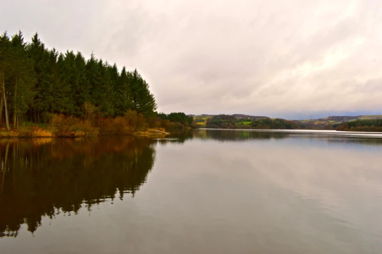 the sky is cloudy over the lake by the woods