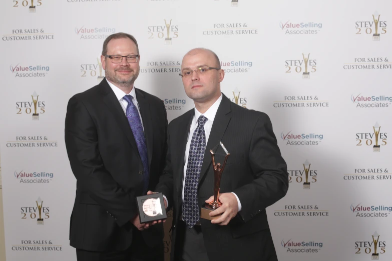 two men in suits holding a award on the red carpet