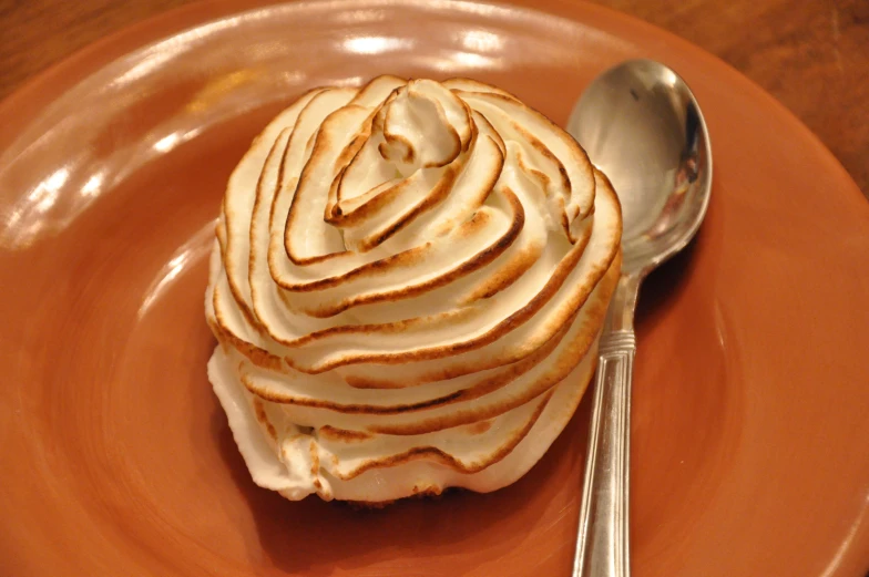 a spoon rests on an orange plate with a pastry