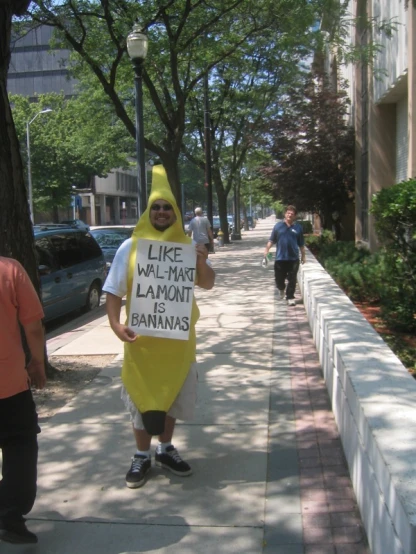 a man walking down the street dressed as a banana holding a sign that says, like we have lanout bananas