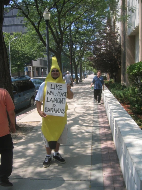 a man walking down the street dressed as a banana holding a sign that says, like we have lanout bananas