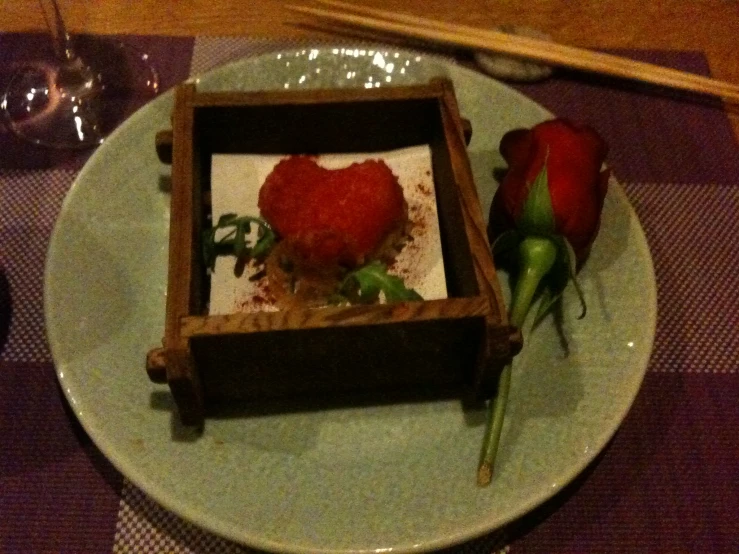 a white plate topped with a red flower and a wooden box