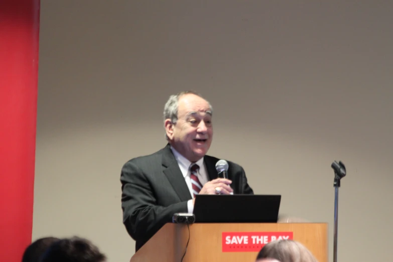 a man in suit and tie speaks at an event