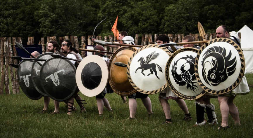 several people in medieval period costumes and shields, both standing on one knee