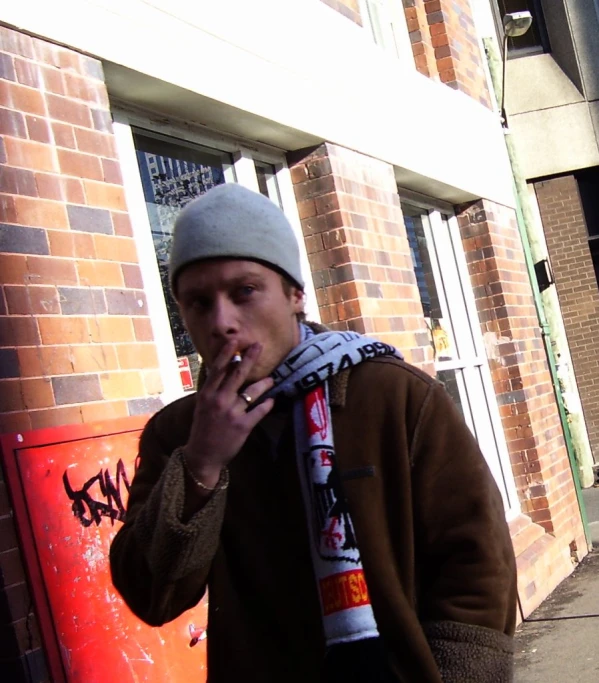 man standing by a brick building smokes and poses