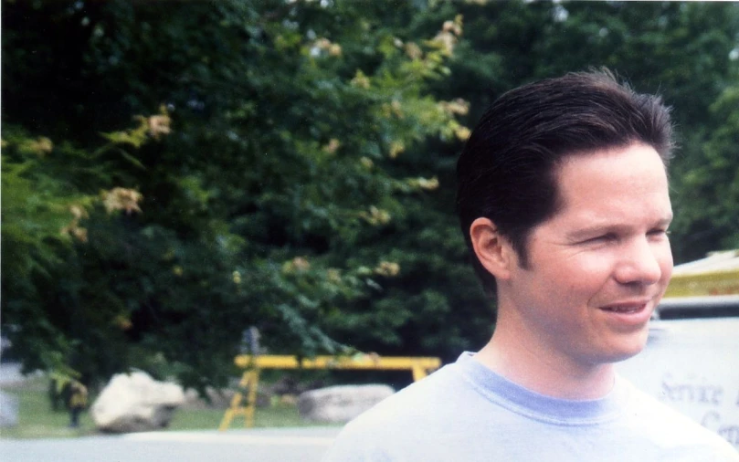 a man wearing a white shirt standing in front of trees