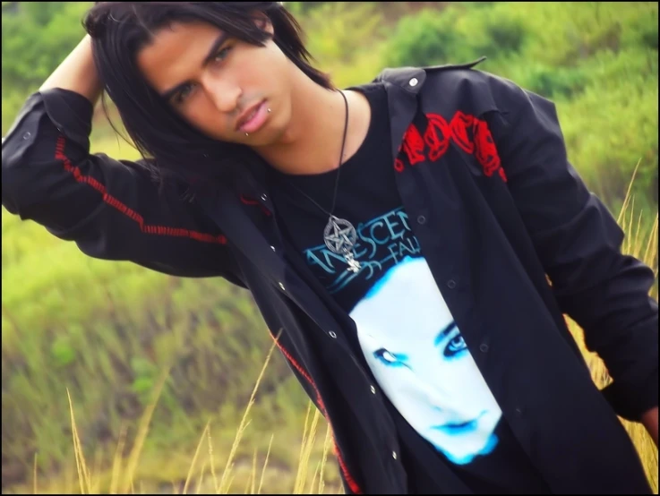 a boy in a black shirt with long hair standing next to a field