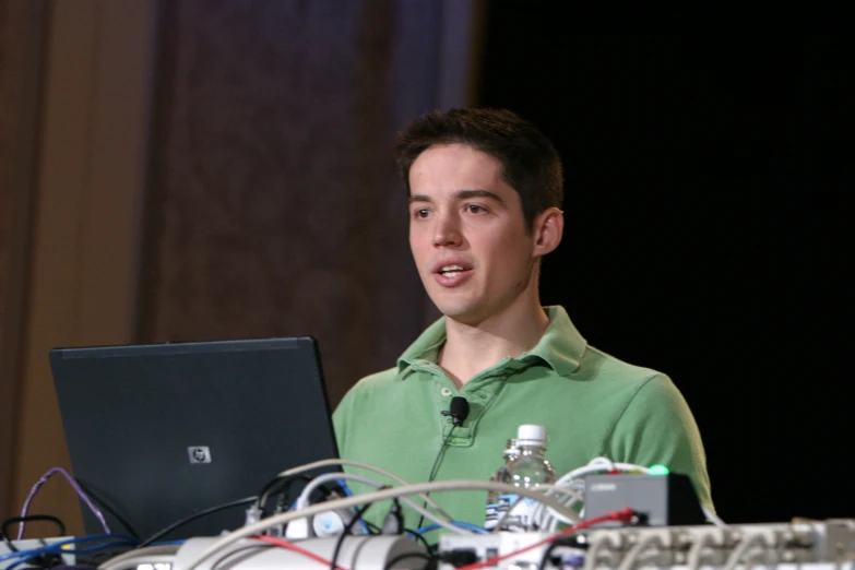 a man stands near wires, electronic equipment and laptop