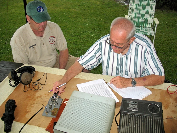 two men sit at a table working on electronics