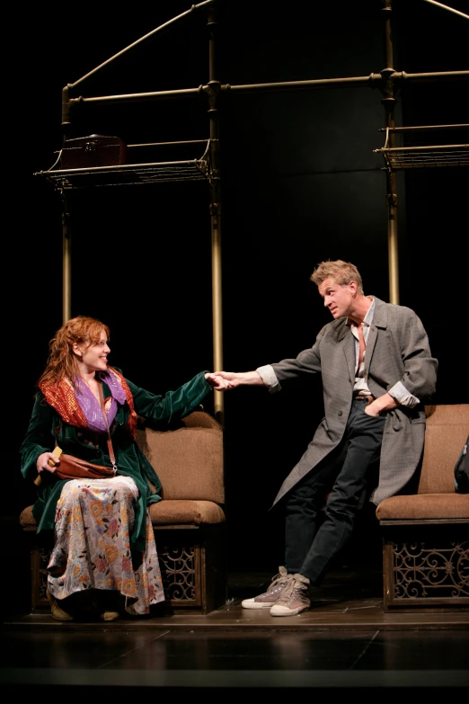 a man in a suit and tie standing next to a woman in a chair