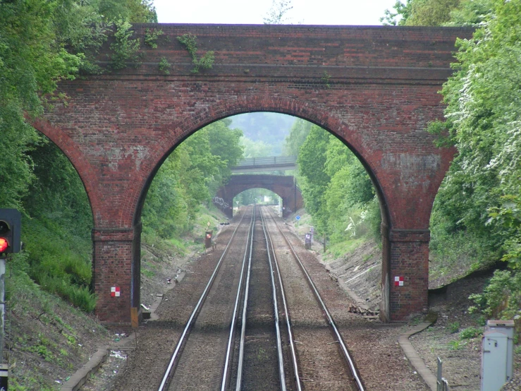 an empty railroad track under an old brick bridge