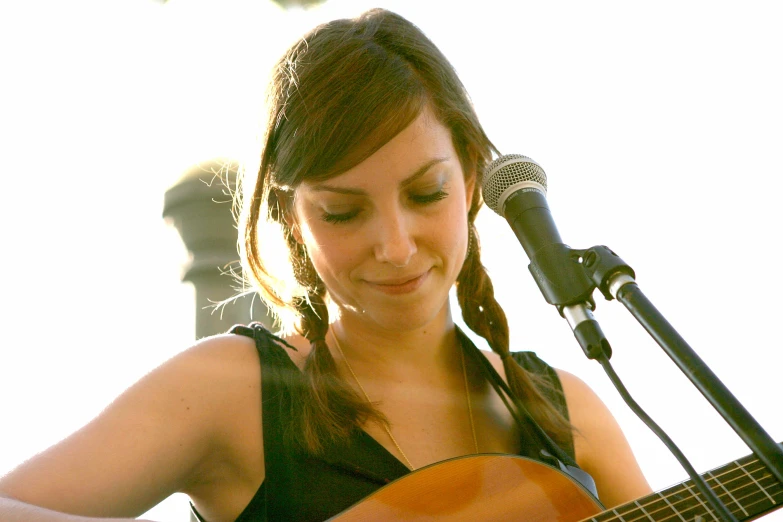 a woman with a guitar and microphone in front of an outdoor stage