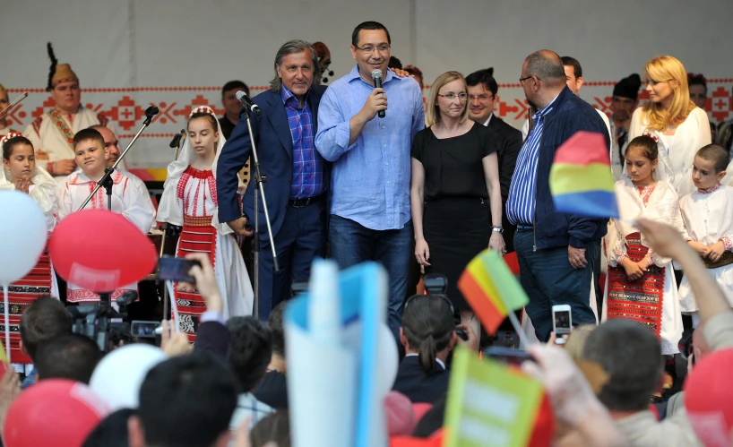 two men speaking in front of people with balloons