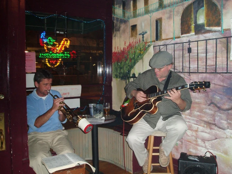 two men sitting on chairs playing instruments in front of a mural