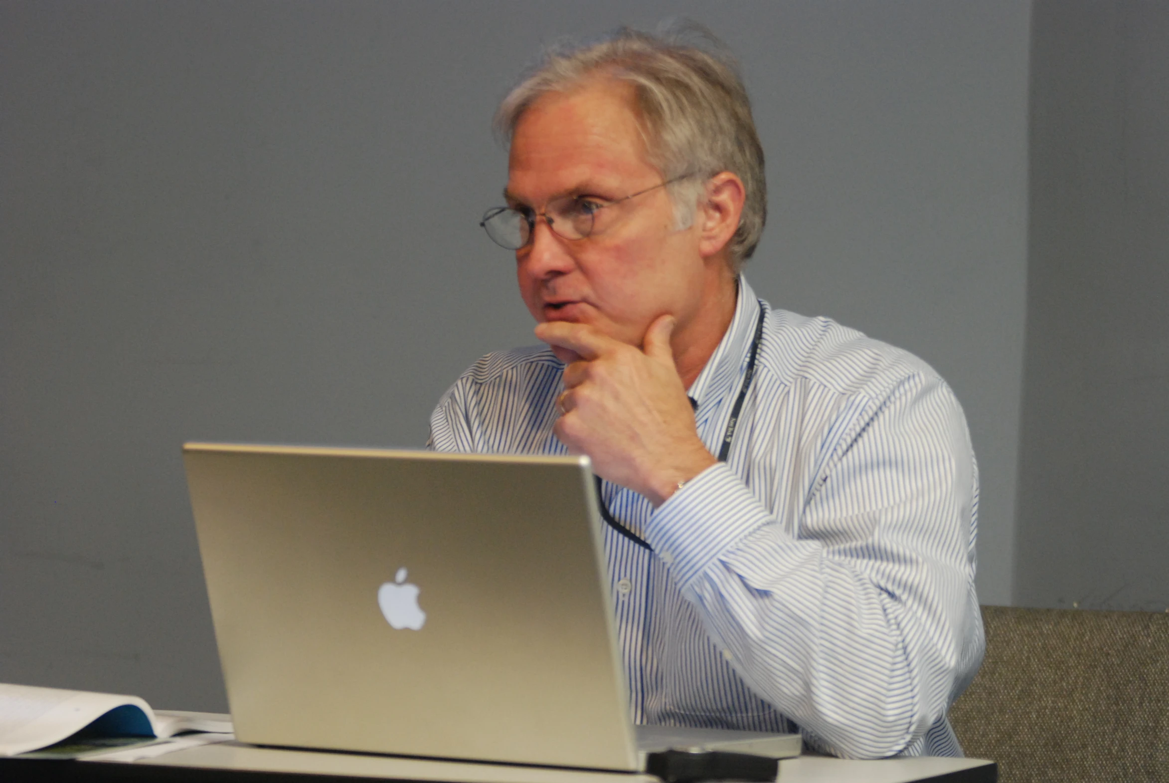 a man wearing glasses, sitting at a table using his laptop